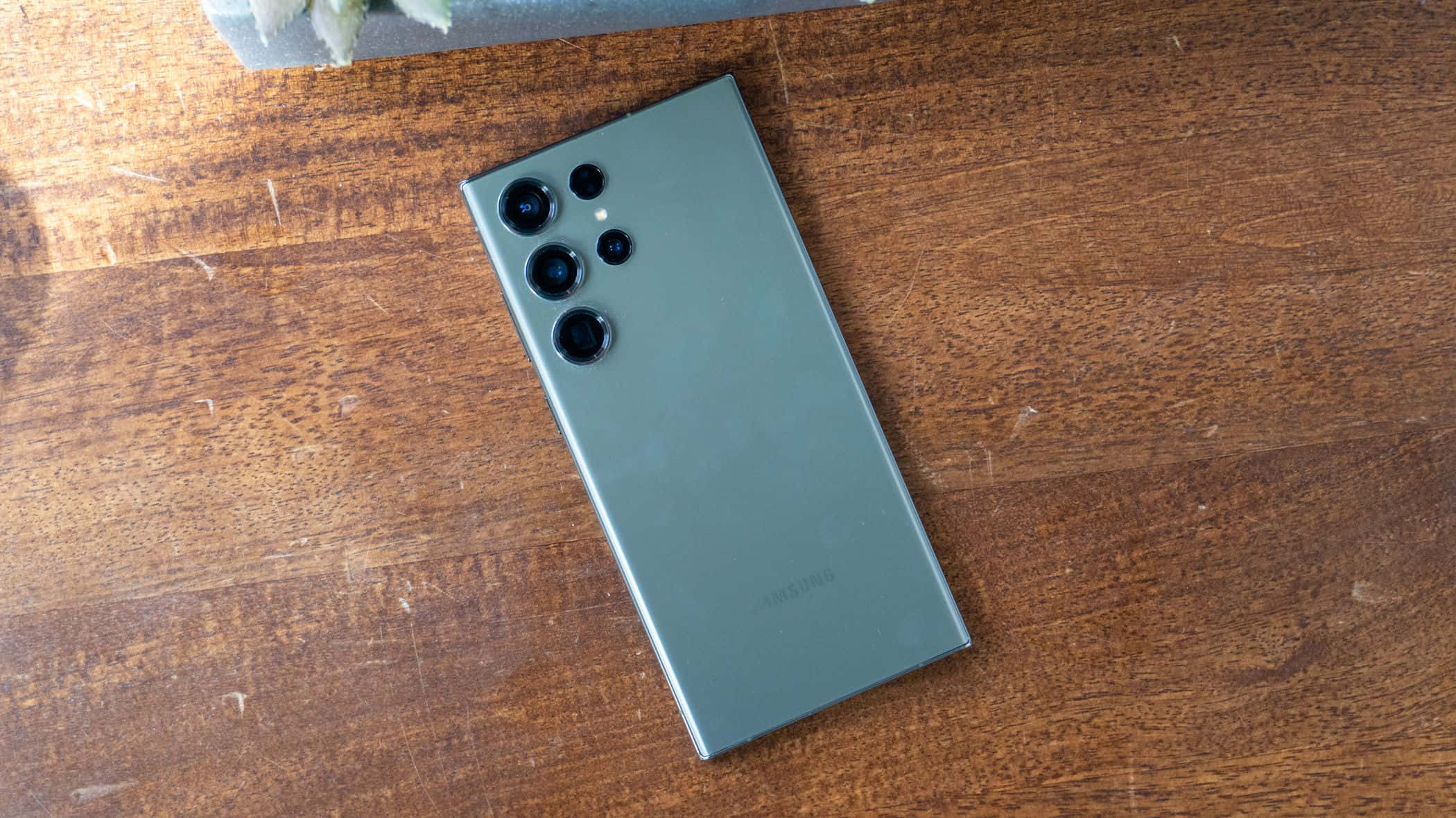 Samsung S23 Ultra зеленая задняя панель с массивом камер на деревянной поверхности Шпалери