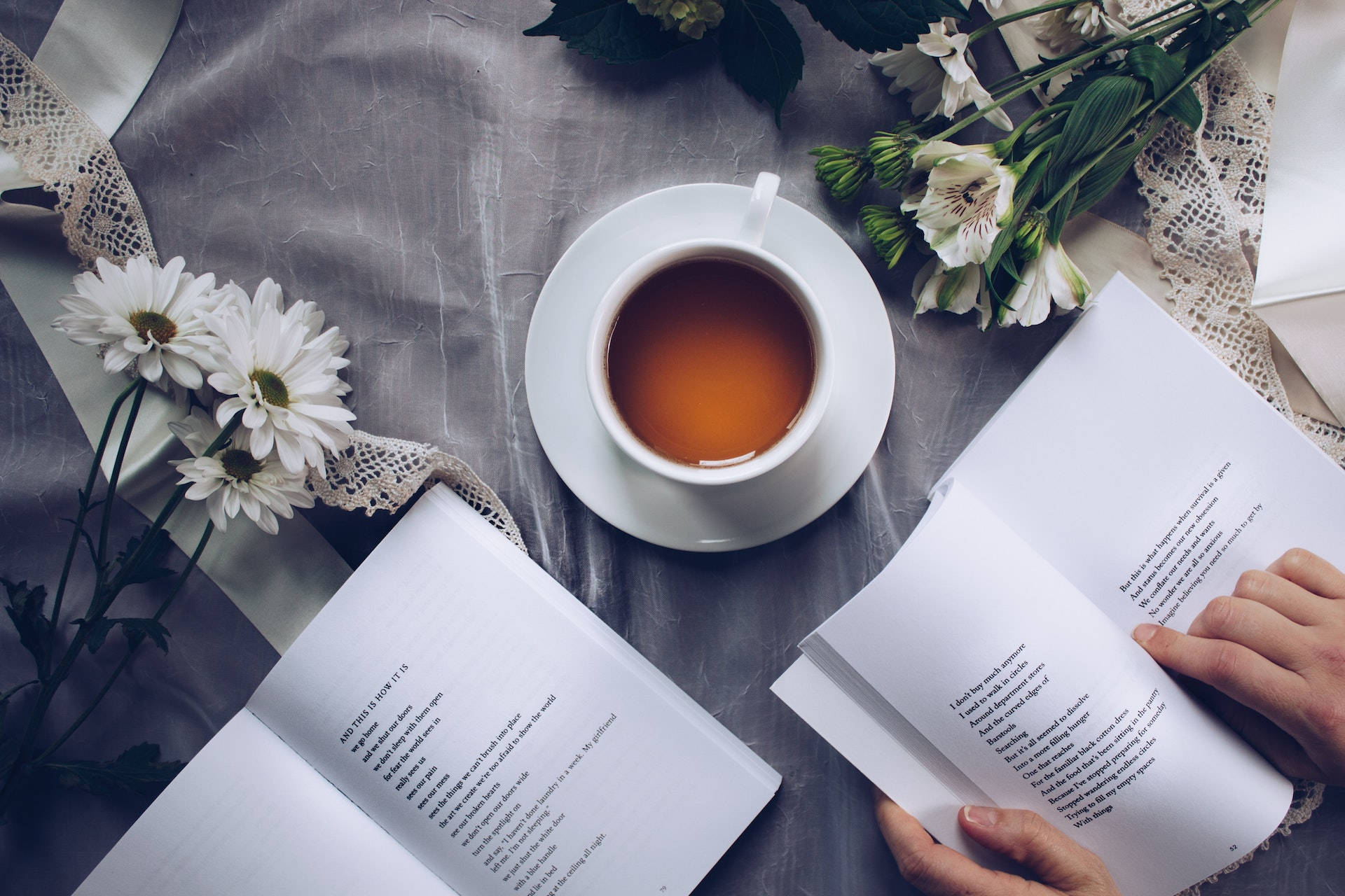Біла керамічна чашка з блюдцем біля двох книг Шпалери