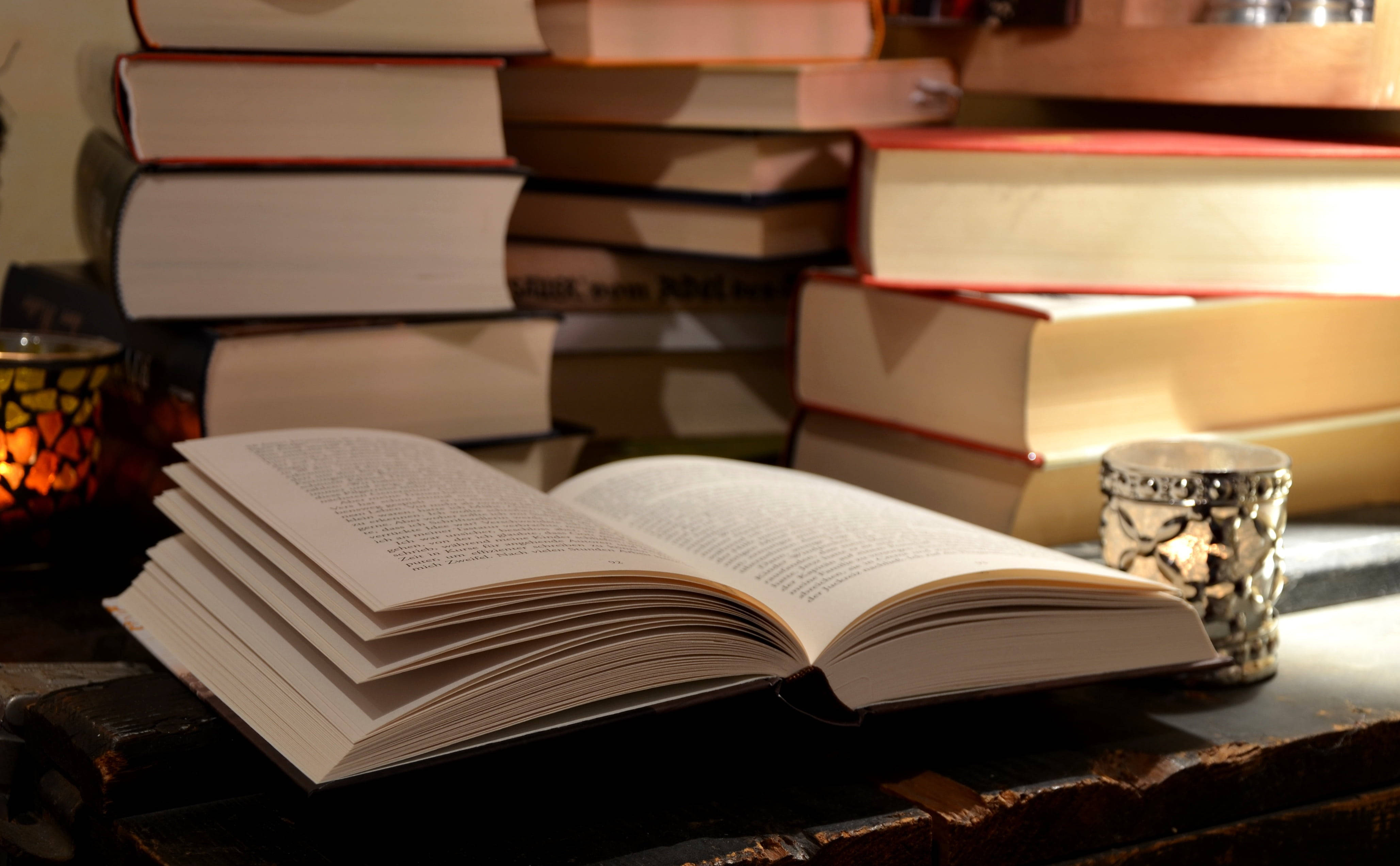 Відкрита книга на письмовому столі в оточенні довідкових книг Шпалери