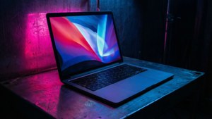 MacBook у стилі кіберпанк з неоновими відблисками у темній кімнаті.